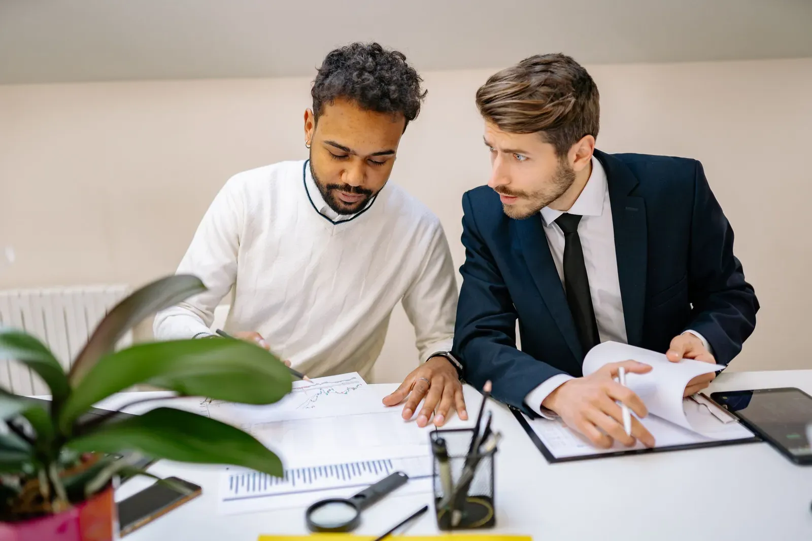Twee collega's aan een bureau nemen samen uitgeprinte overzichten met grafieken door