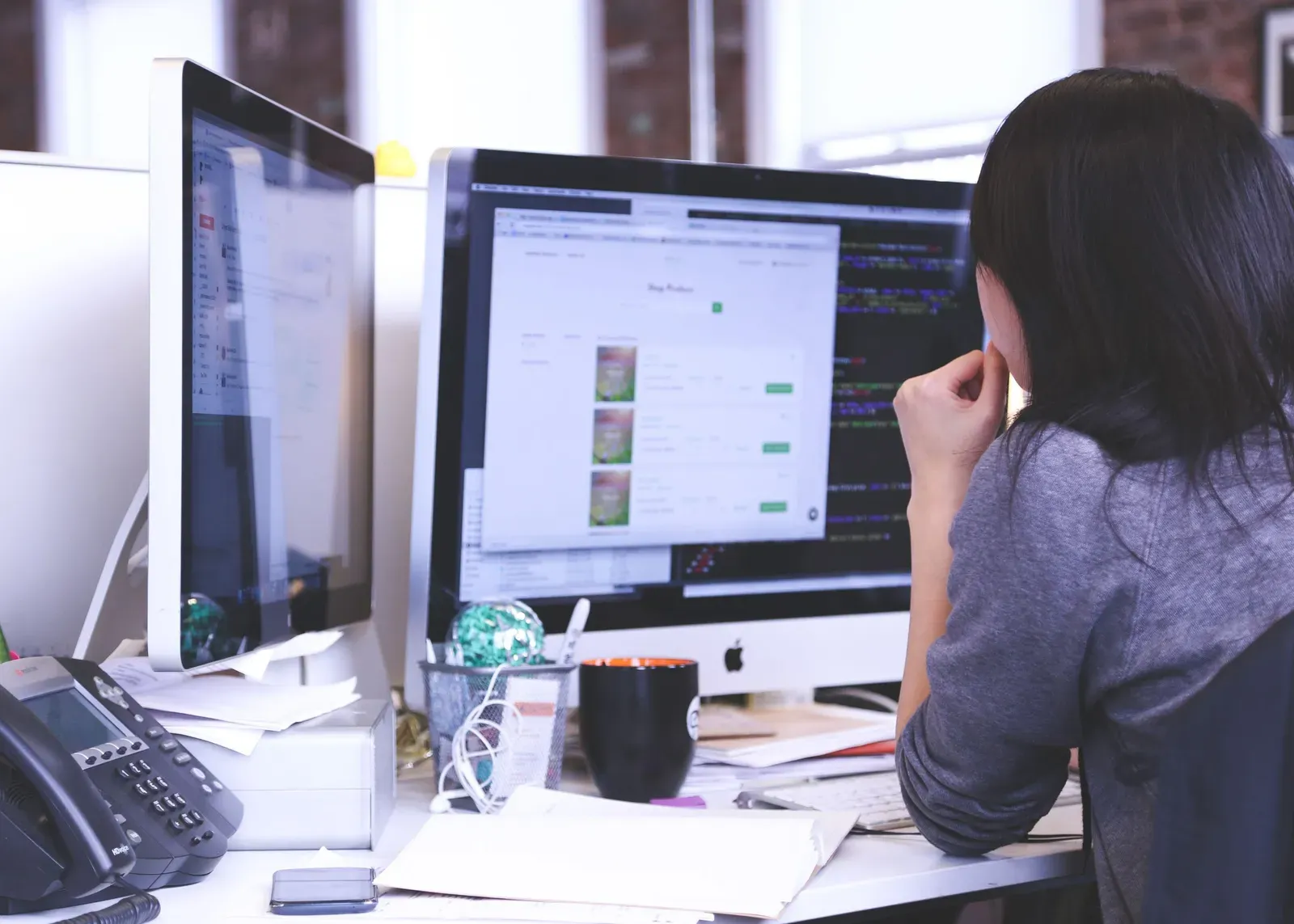 Vrouw achter twee beeldschermen werkt aan haar bureau in een zakelijke webapplicatie