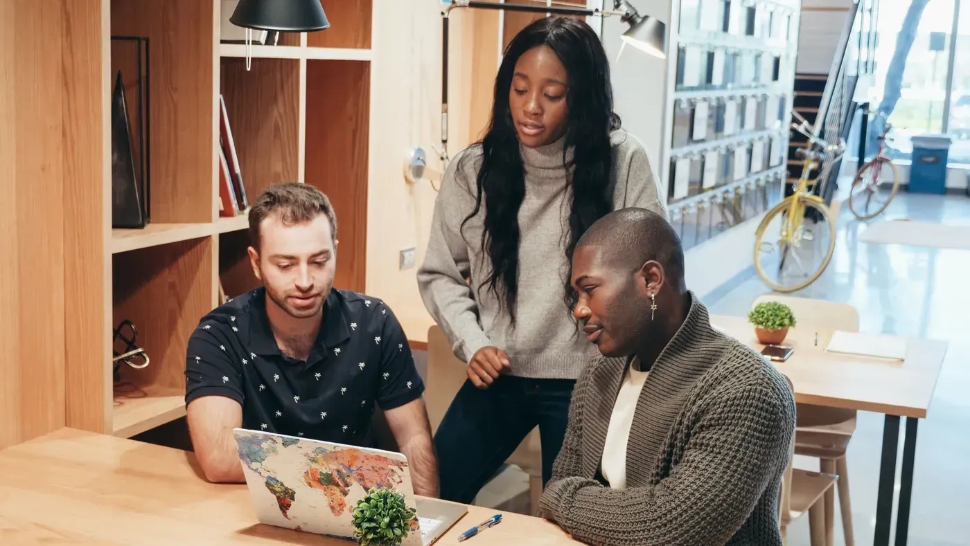 Three colleagues look at a laptop together while one of them points at something