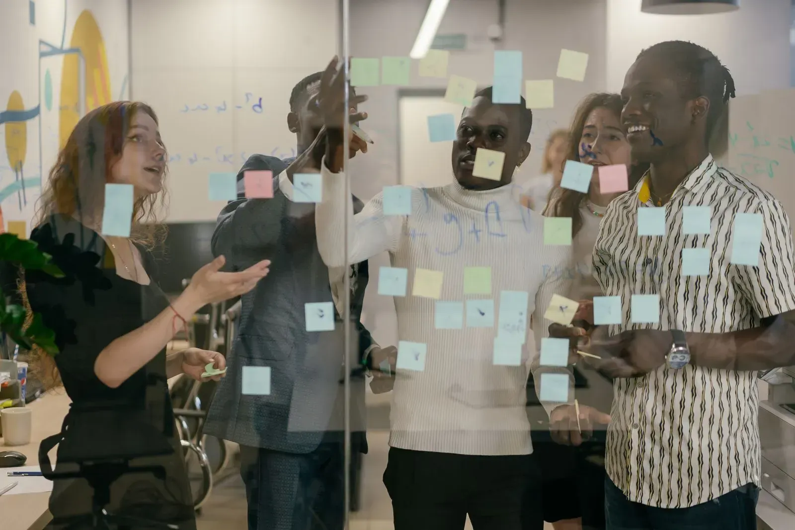 Four colleagues sticking yellow and blue sticky notes on a glass wall and discussing their order