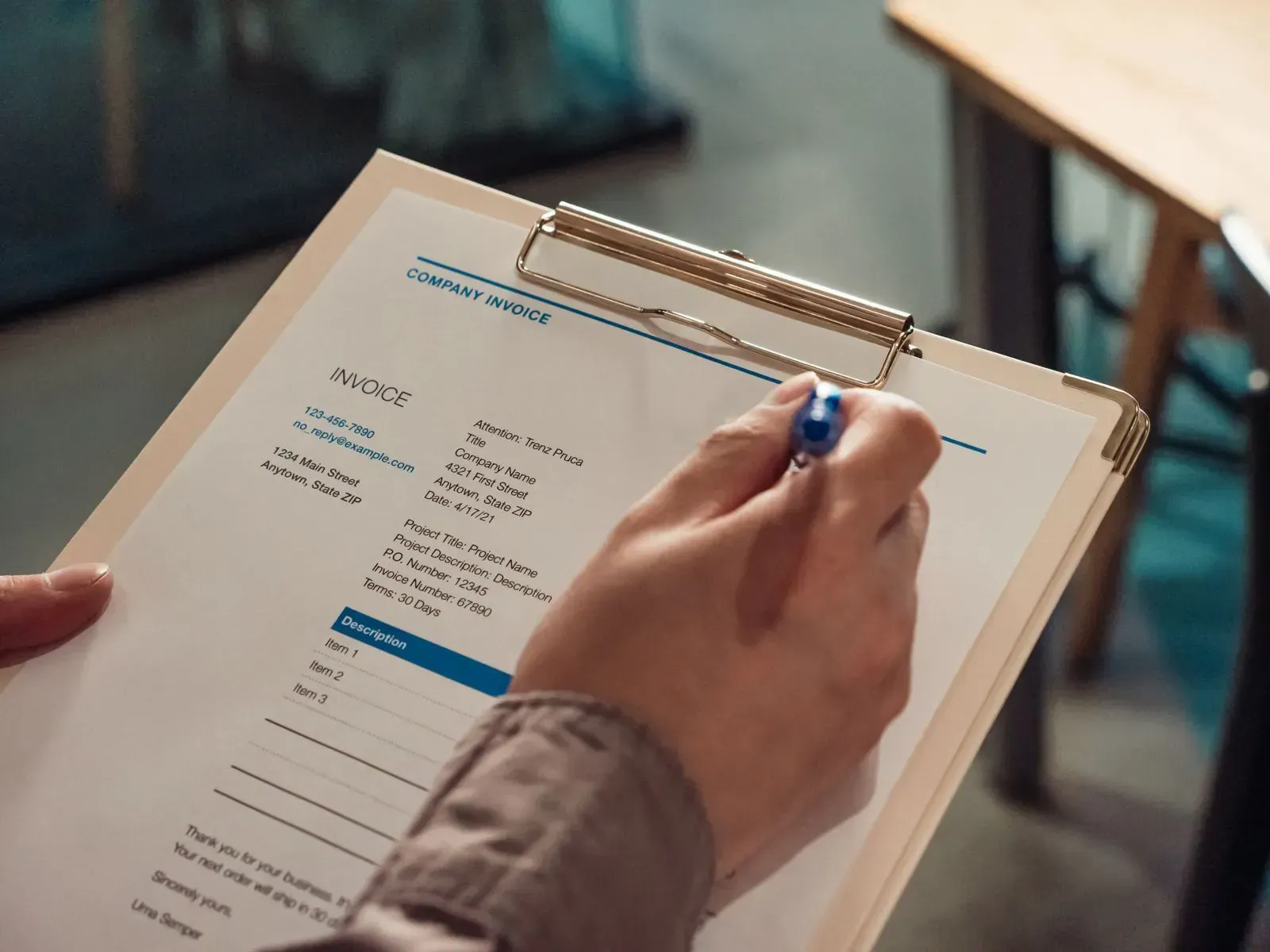 A hand holding a pen checks an invoice on a clipboard line by line