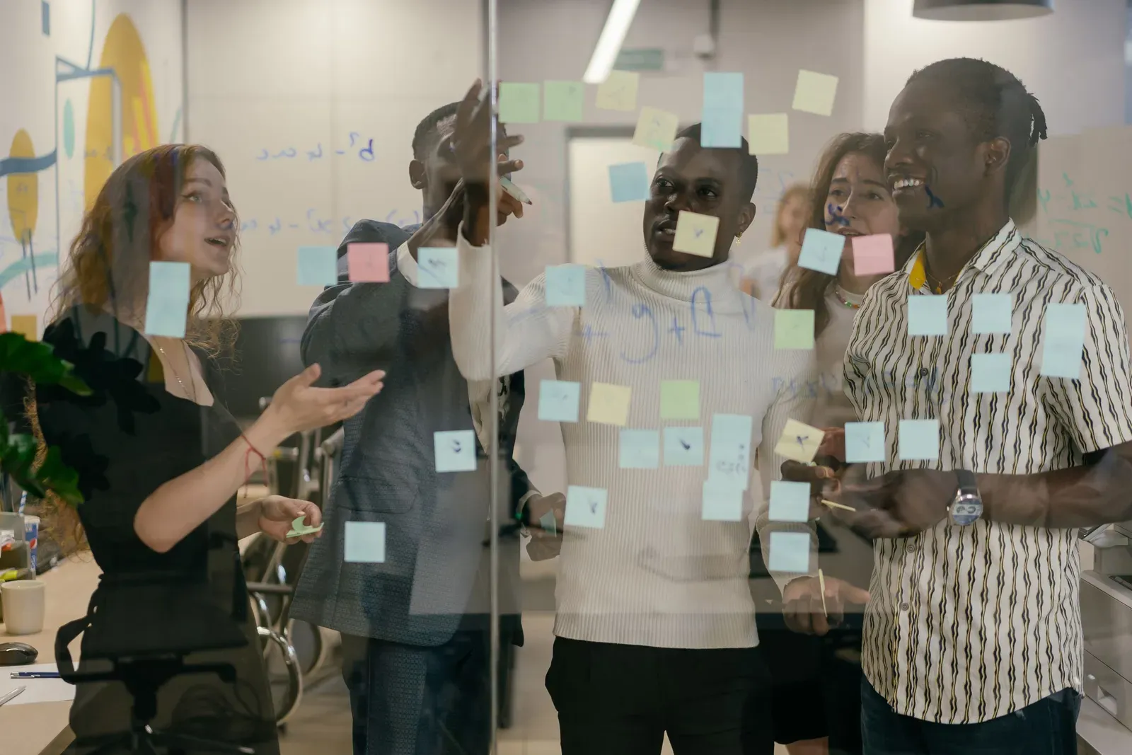 Five colleagues standing at a glass wall working out a plan with coloured sticky notes
