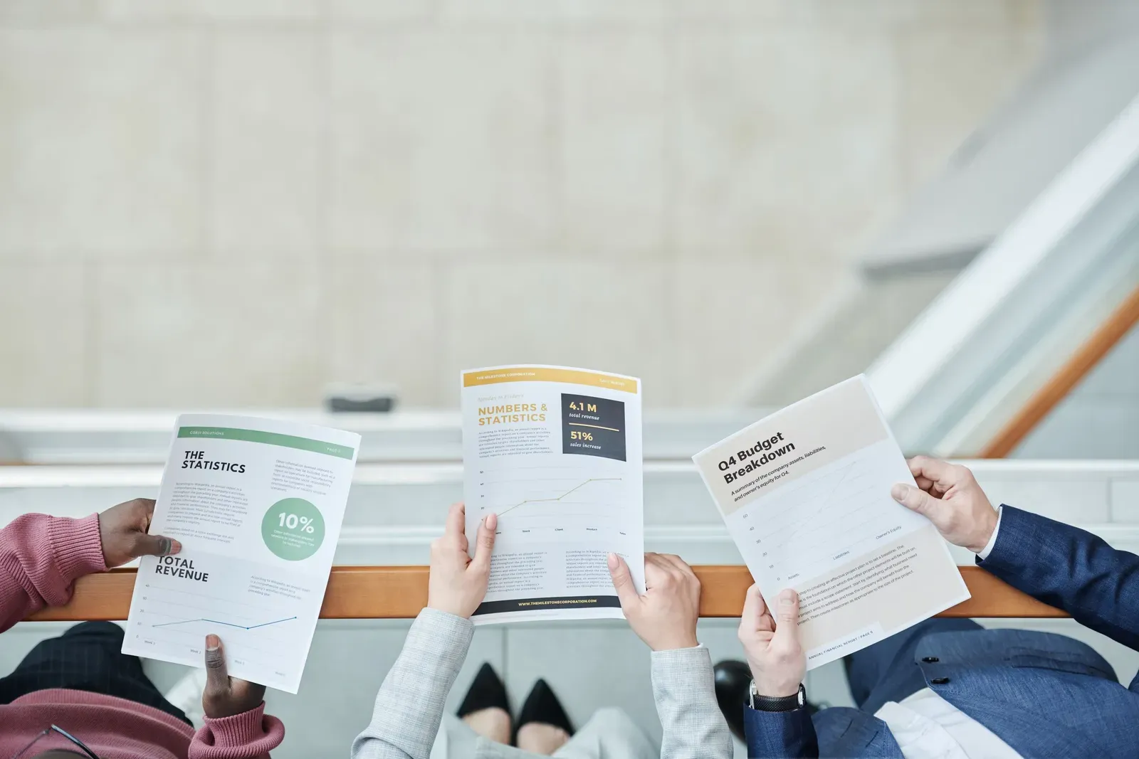 Three colleagues each holding up a different printed report showing revenue and budget figures