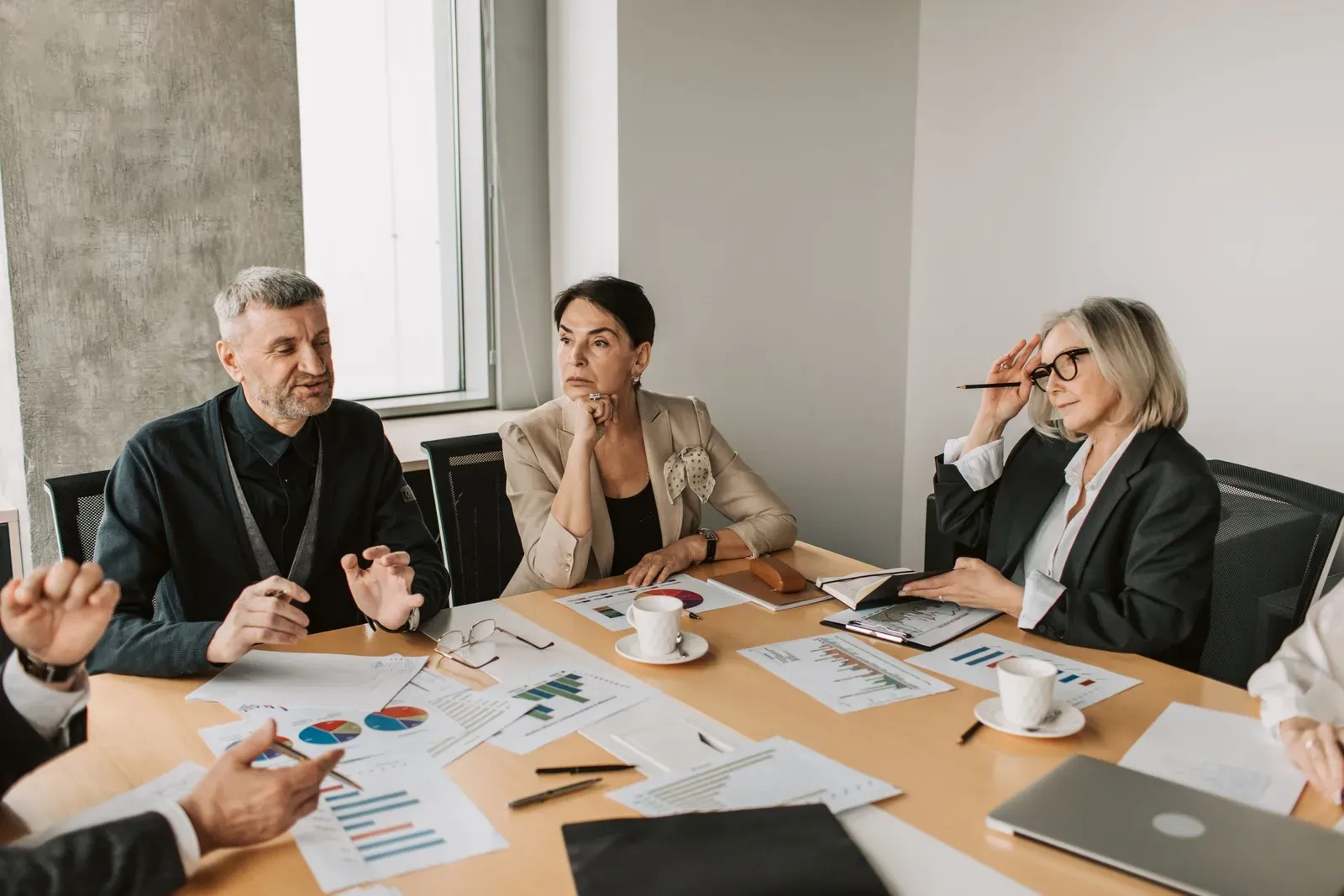 Four colleagues in discussion at a meeting table with printed charts and coffee cups in front of them