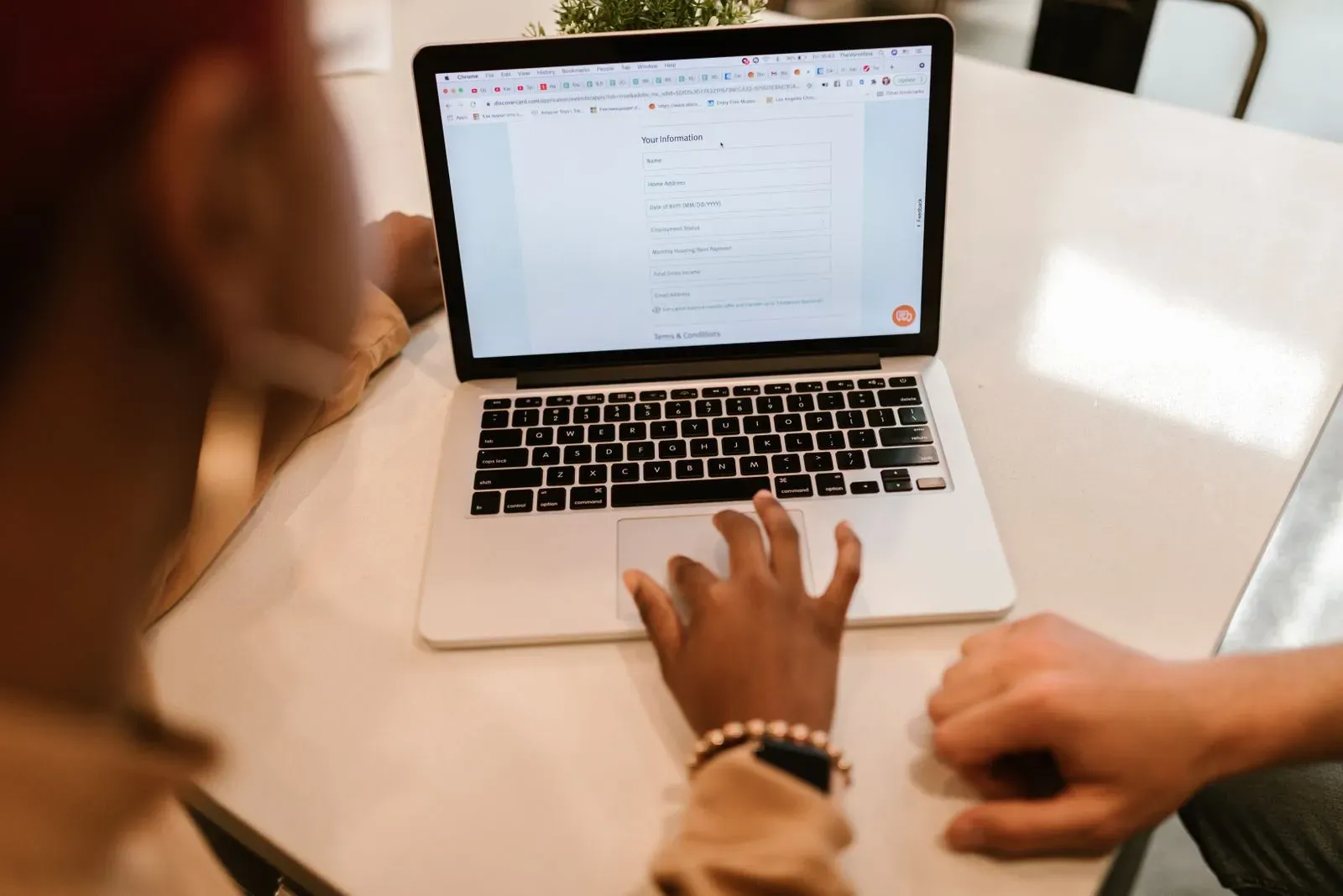 Two people at a table filling in an online form together on a laptop