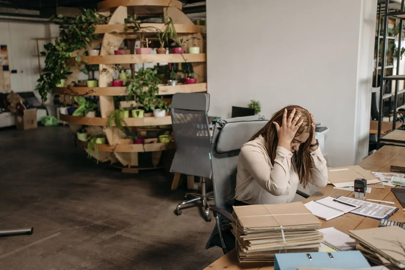 Woman at a desk with her hands in her hair, next to stacks of files and papers