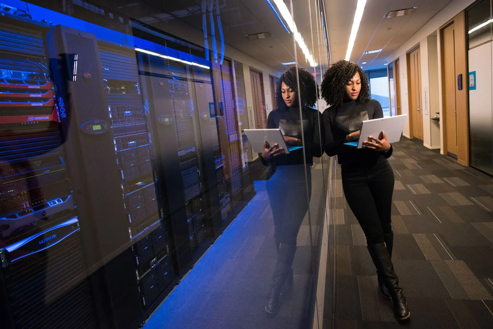 Vrouw met laptop loopt langs de serverkasten van een datacenter