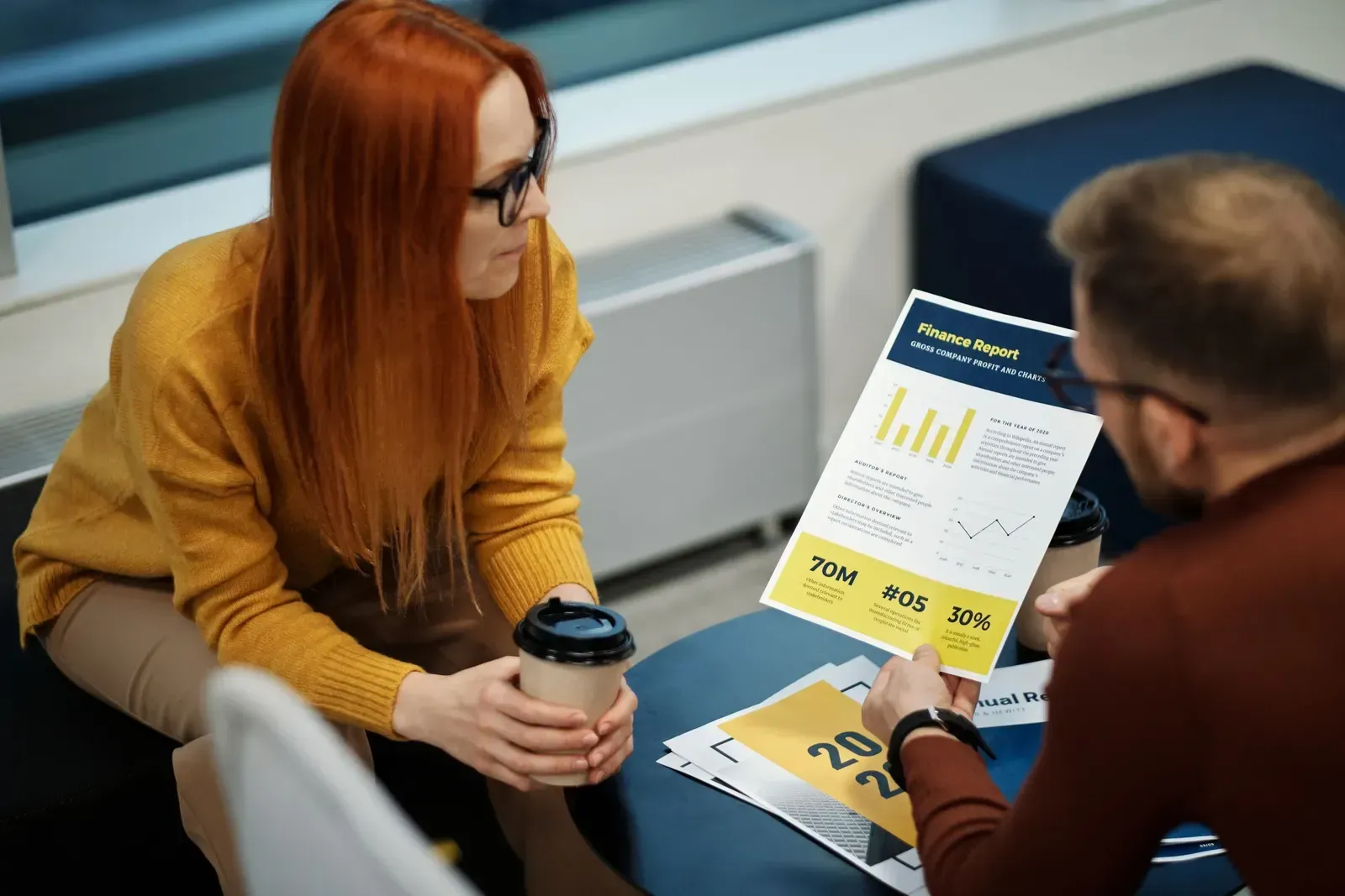 Twee collega's aan een tafel bekijken een uitgeprint financieel rapport met grafieken en kerncijfers
