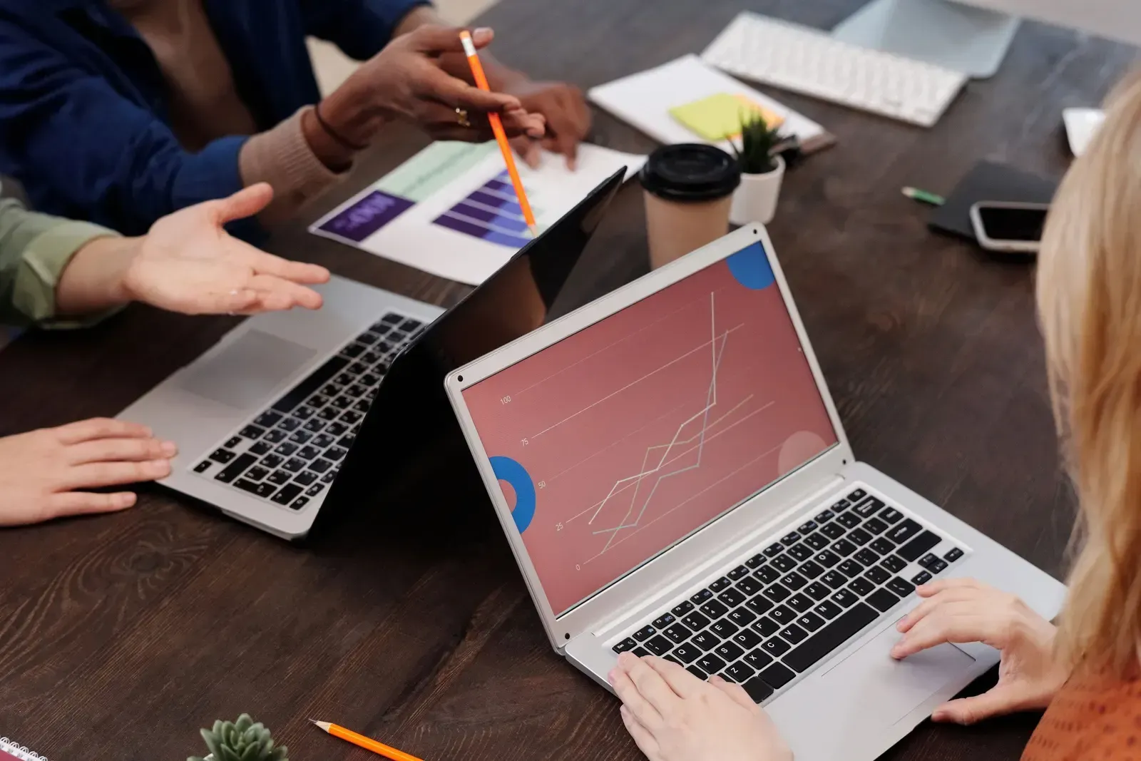 Collega's wijzen naar grafieken op papier en op een laptopscherm tijdens een overleg aan tafel