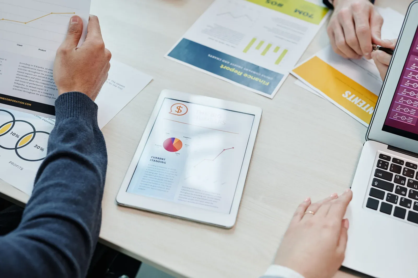 Two colleagues at a table with printed financial reports and a tablet showing the same figures overview