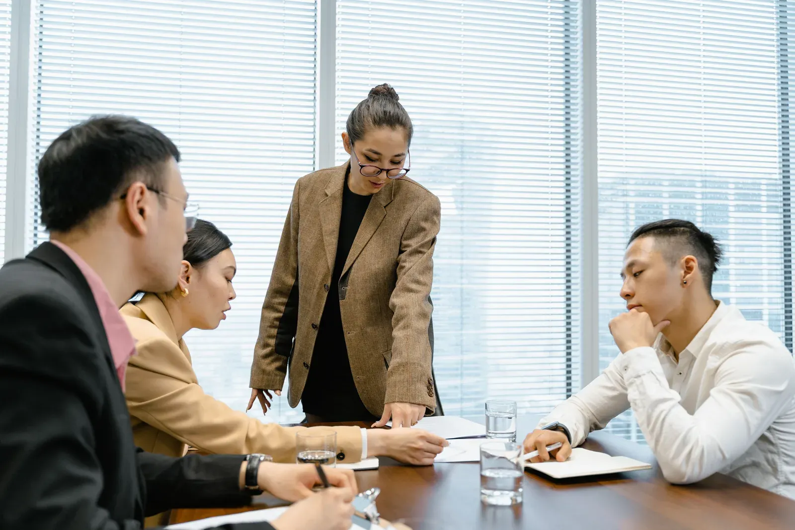 Staande collega wijst naar een document op de vergadertafel terwijl drie mensen meekijken
