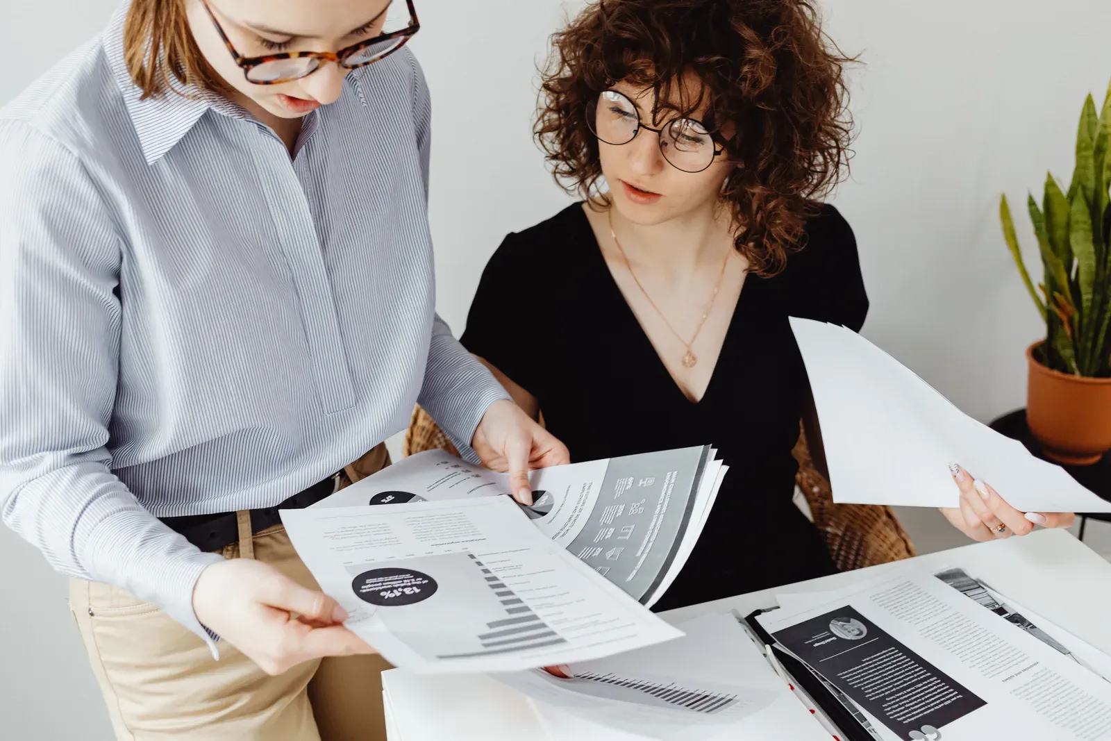 Twee collega's vergelijken staand een aantal uitgeprinte rapporten met grafieken en wijzen naar een cijfer