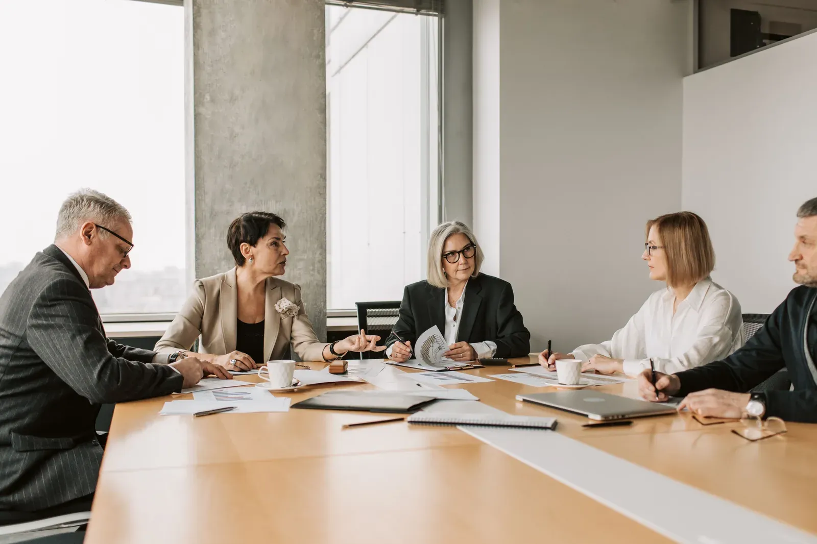 Vijf collega's in een vergaderruimte bespreken uitgeprinte overzichten die op tafel liggen
