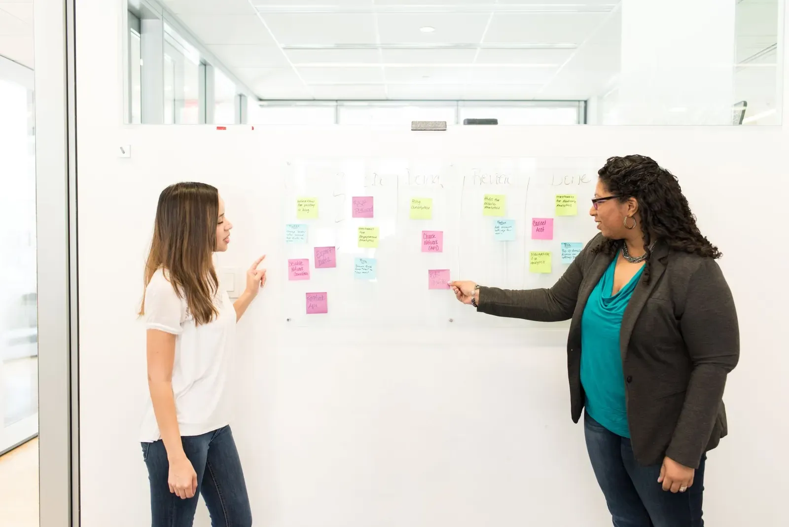 Twee vrouwen voor een whiteboard vol gekleurde sticky notes, een van hen wijst een briefje aan