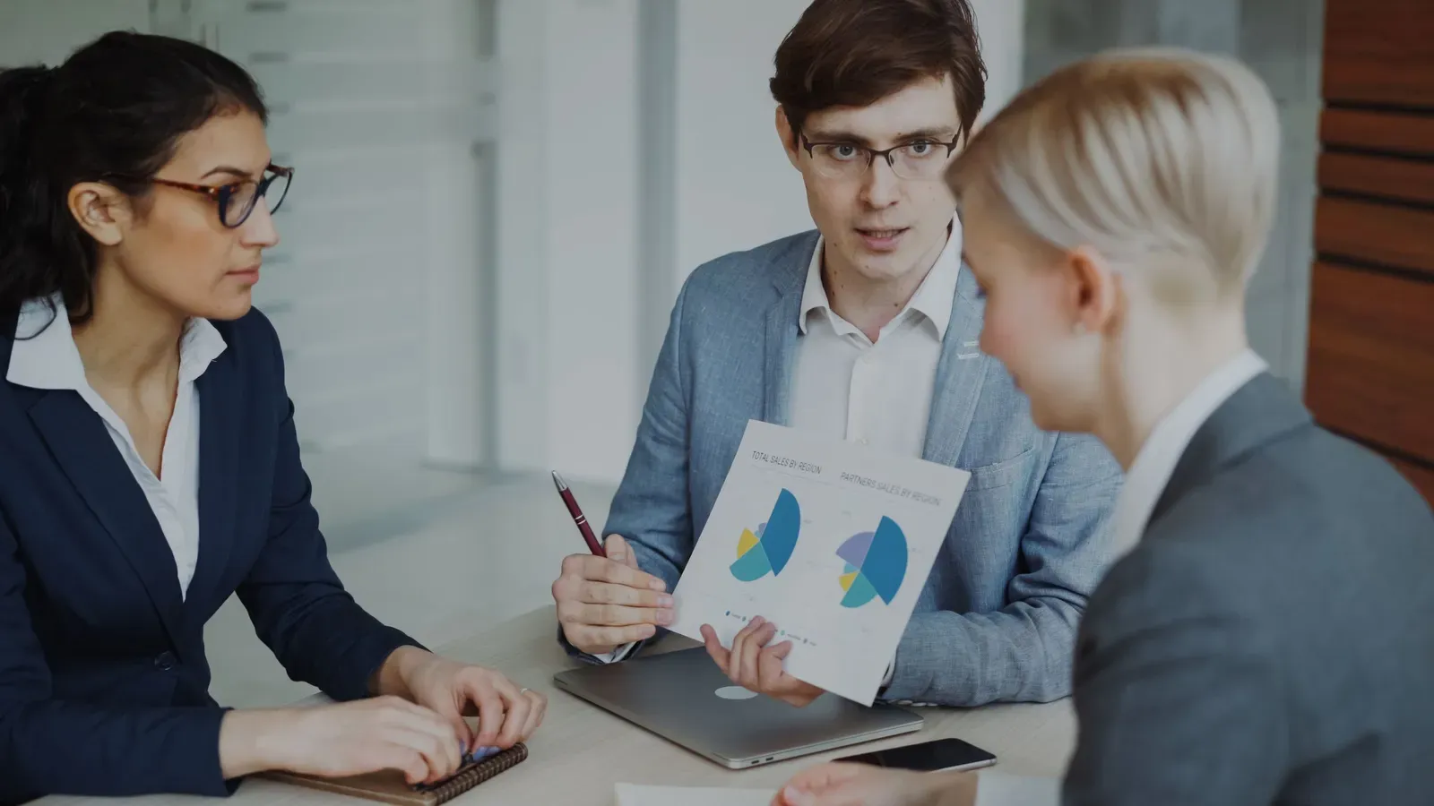 Drie collega's aan een vergadertafel bespreken een uitgeprint overzicht met cirkeldiagrammen