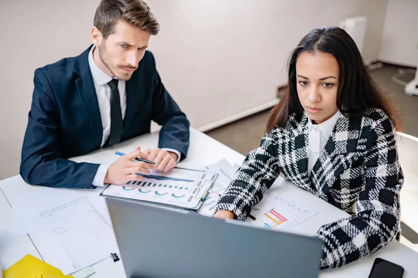 Twee collega's aan een bureau nemen samen uitgeprinte grafieken en een laptopscherm door
